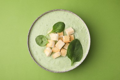 Photo of Delicious spinach cream soup with leaves and croutons in bowl on green background, top view