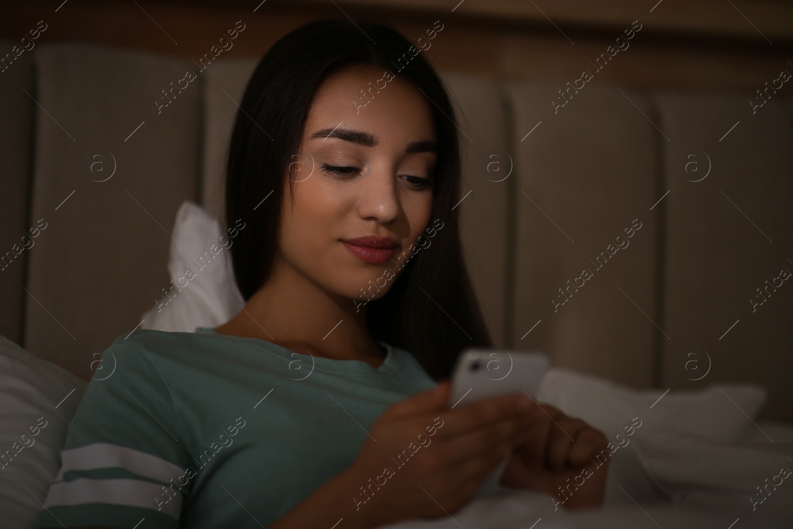 Photo of Young woman with nomophobia using smartphone in bed at night. Insomnia concept