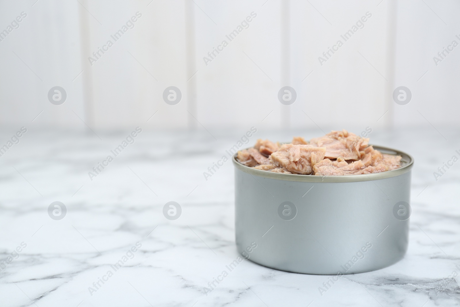 Photo of Tin can with canned tuna on white marble table, space for text