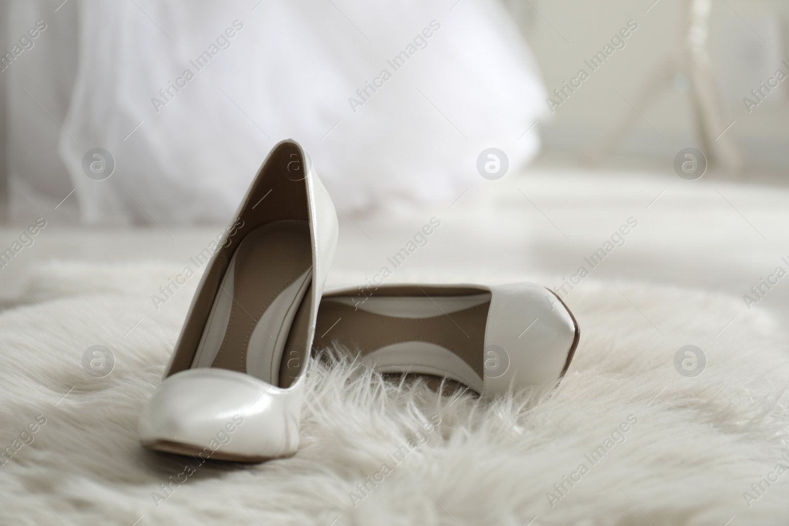 Photo of White wedding shoes on furry rug in room