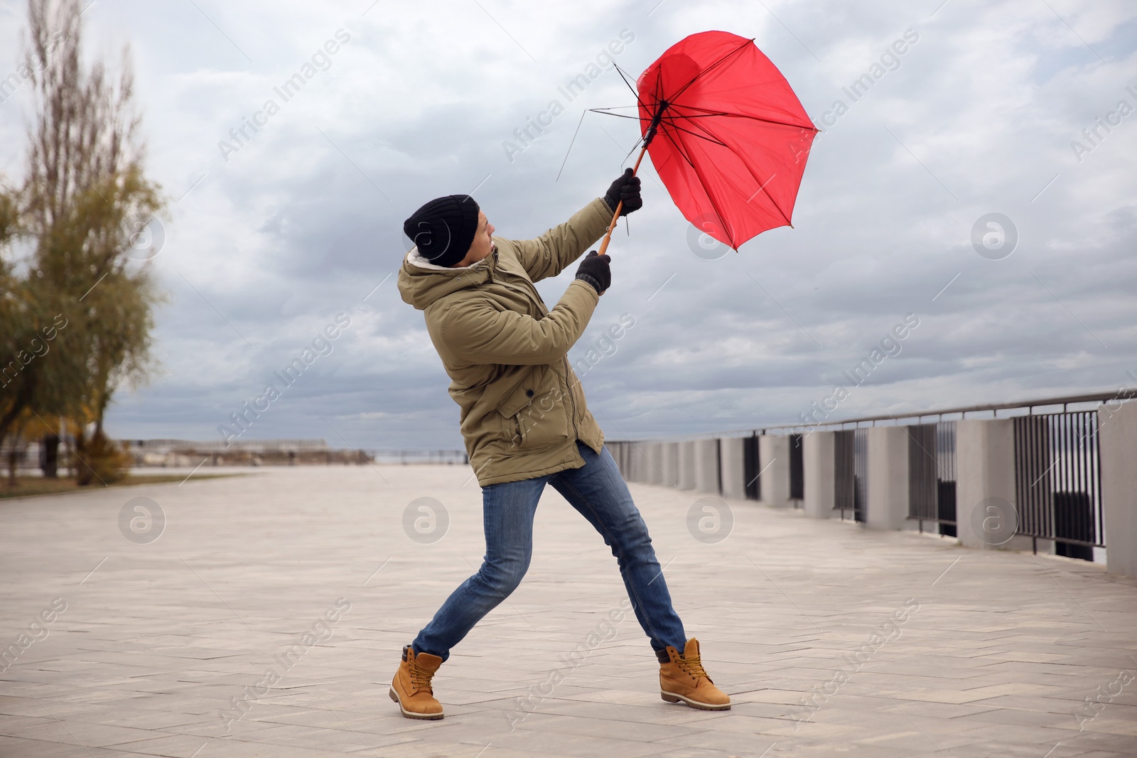Photo of Man with red umbrella caught in gust of wind outdoors
