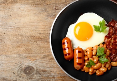 Photo of Frying pan with traditional English breakfast on wooden table, top view. Space for text