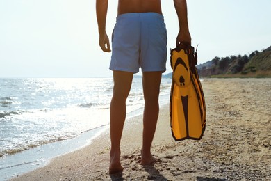 Photo of Back view of man with flippers walking on beach, closeup