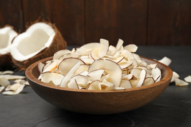 Photo of Tasty coconut chips in bowl on black table