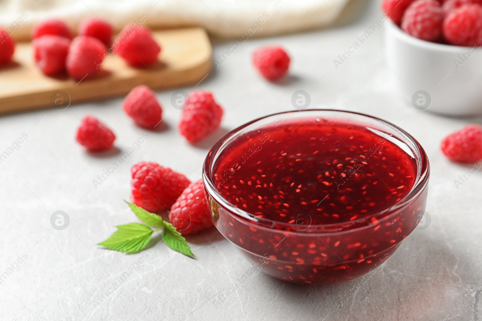 Photo of Bowl of sweet jam with ripe raspberries on white table, closeup. Space for text