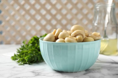 Photo of Tasty marinated mushrooms in bowl on white marble table, closeup