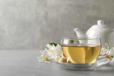 Glass cup of jasmine tea and fresh flowers on grey table. Space for text