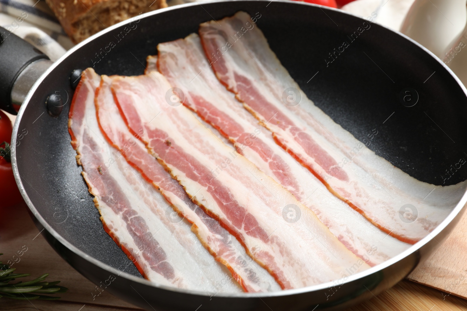 Photo of Slices of raw bacon in frying pan on table, closeup