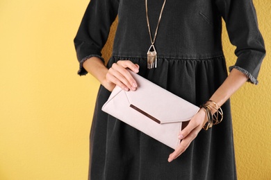 Young woman in stylish outfit with purse on color background, closeup