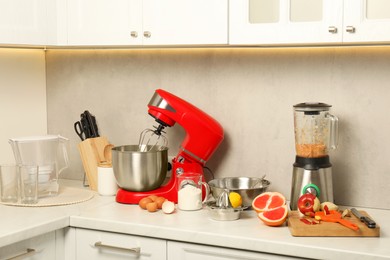 Photo of Modern red stand mixer, blender and different ingredients on white marble countertop in kitchen