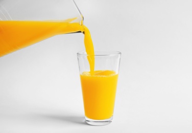 Pouring fresh orange juice into glass on white background