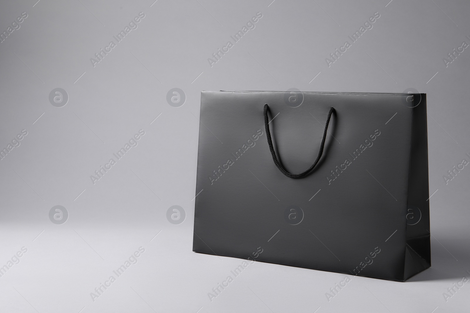 Photo of Black paper bag on light grey background, space for text