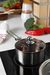 Photo of Metal saucepan on cooktop in kitchen. Cooking utensils