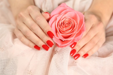 Woman holding manicured hands with red nail polish near rose on fabric, closeup