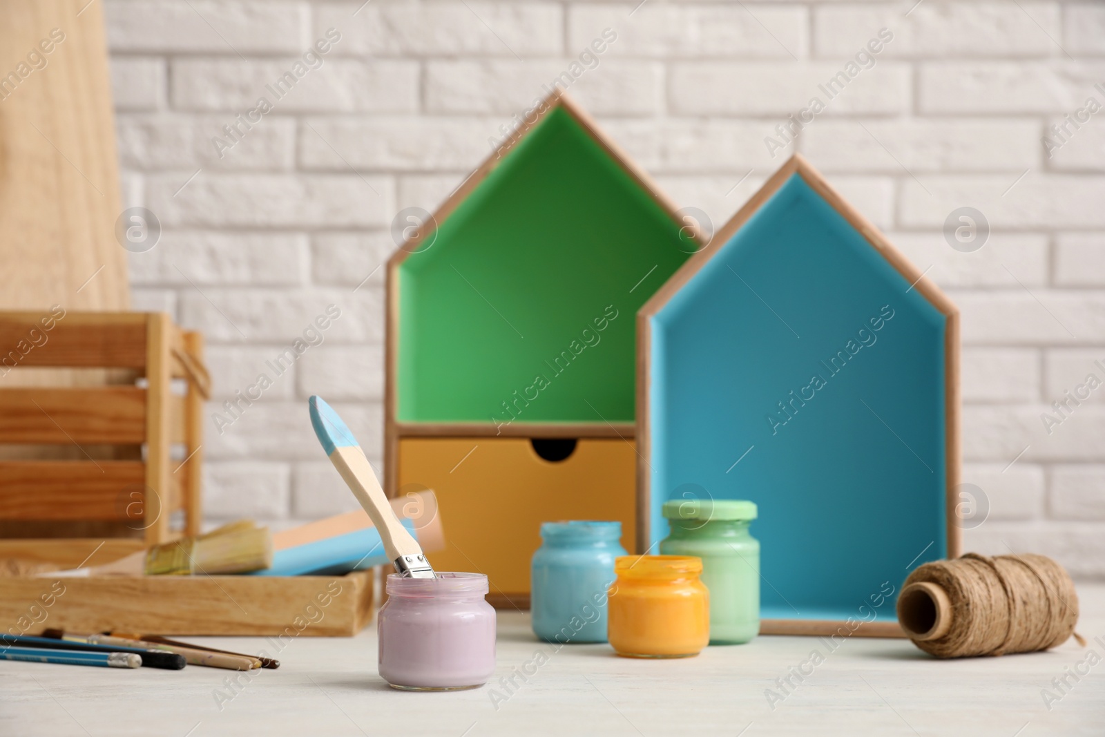 Photo of Jars of paints and decorator tools on white table against brick wall. Interior elements