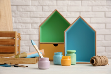 Photo of Jars of paints and decorator tools on white table against brick wall. Interior elements