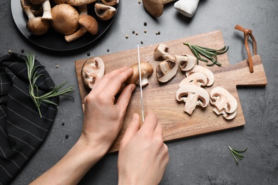 Photo of Woman cutting fresh wild mushrooms at grey table, top view