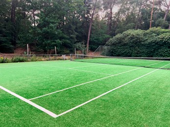 Photo of Tennis court with green grass and net outdoors