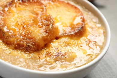 Photo of Tasty homemade french onion soup served in ceramic bowl, closeup