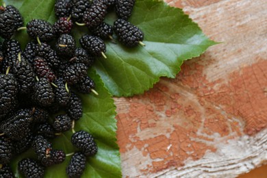 Heap of delicious ripe black mulberries and green leaves on wooden table, flat lay. Space for text