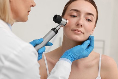 Dermatologist with dermatoscope examining patient`s face in clinic, closeup