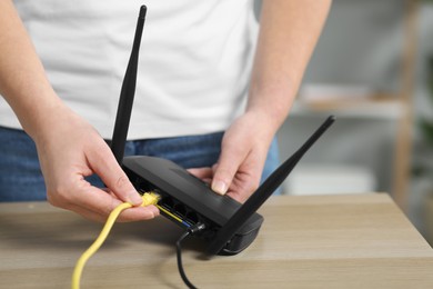 Photo of Woman inserting ethernet cable into Wi-Fi router at table indoors, closeup