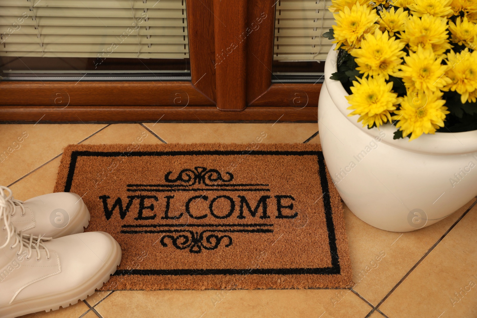 Photo of Door mat with word Welcome, stylish boots and beautiful flowers on floor