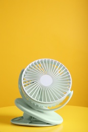 Photo of Modern electric fan on table against yellow background