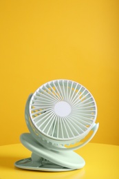 Modern electric fan on table against yellow background