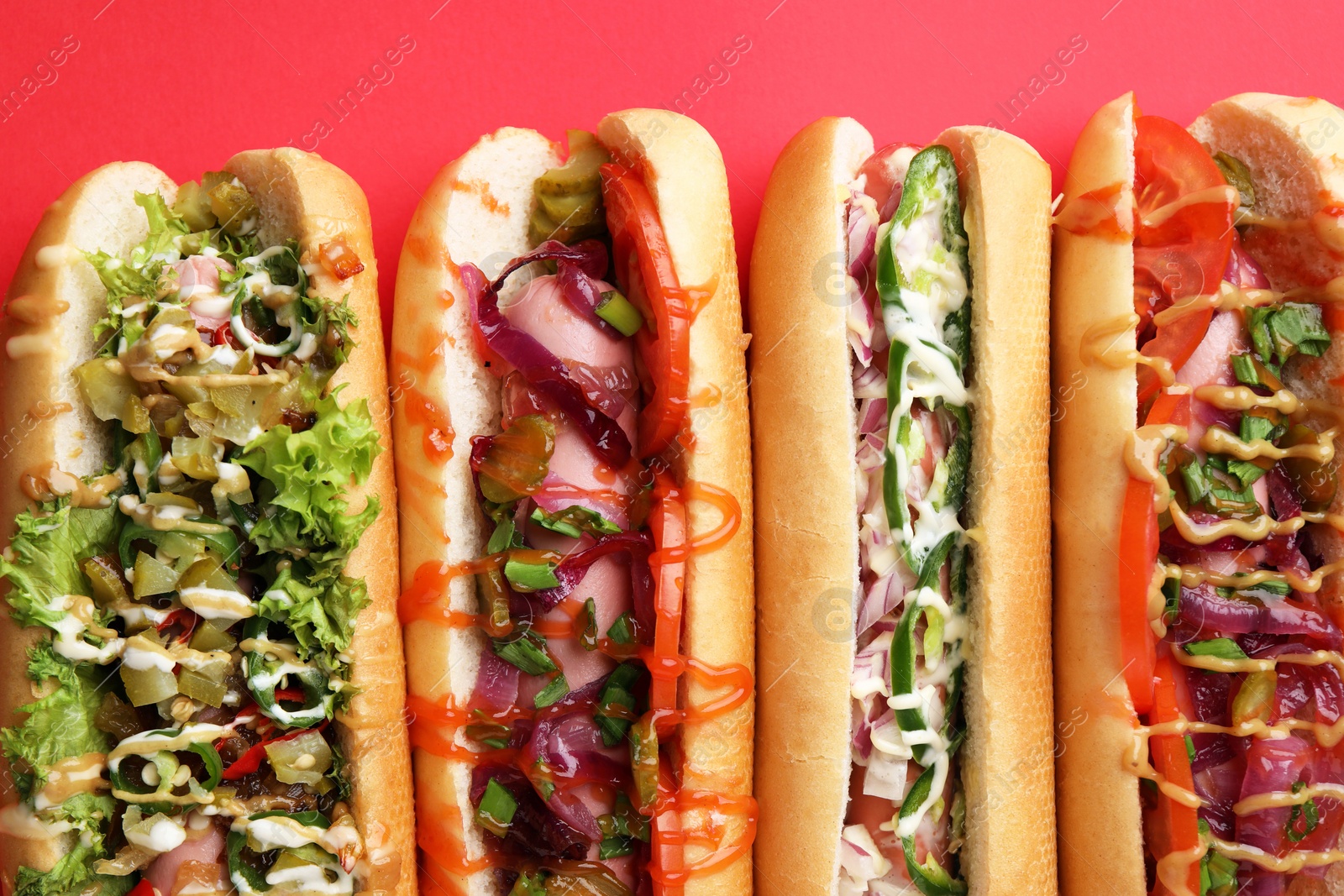 Photo of Delicious hot dogs with different toppings on red background, flat lay