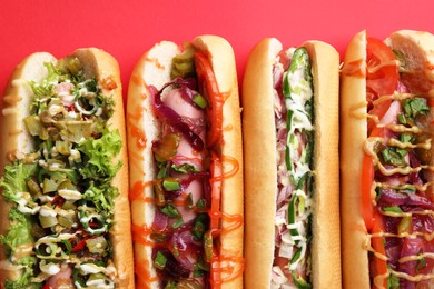 Photo of Delicious hot dogs with different toppings on red background, flat lay
