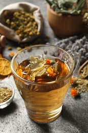 Photo of Freshly brewed tea and dried herbs on grey table