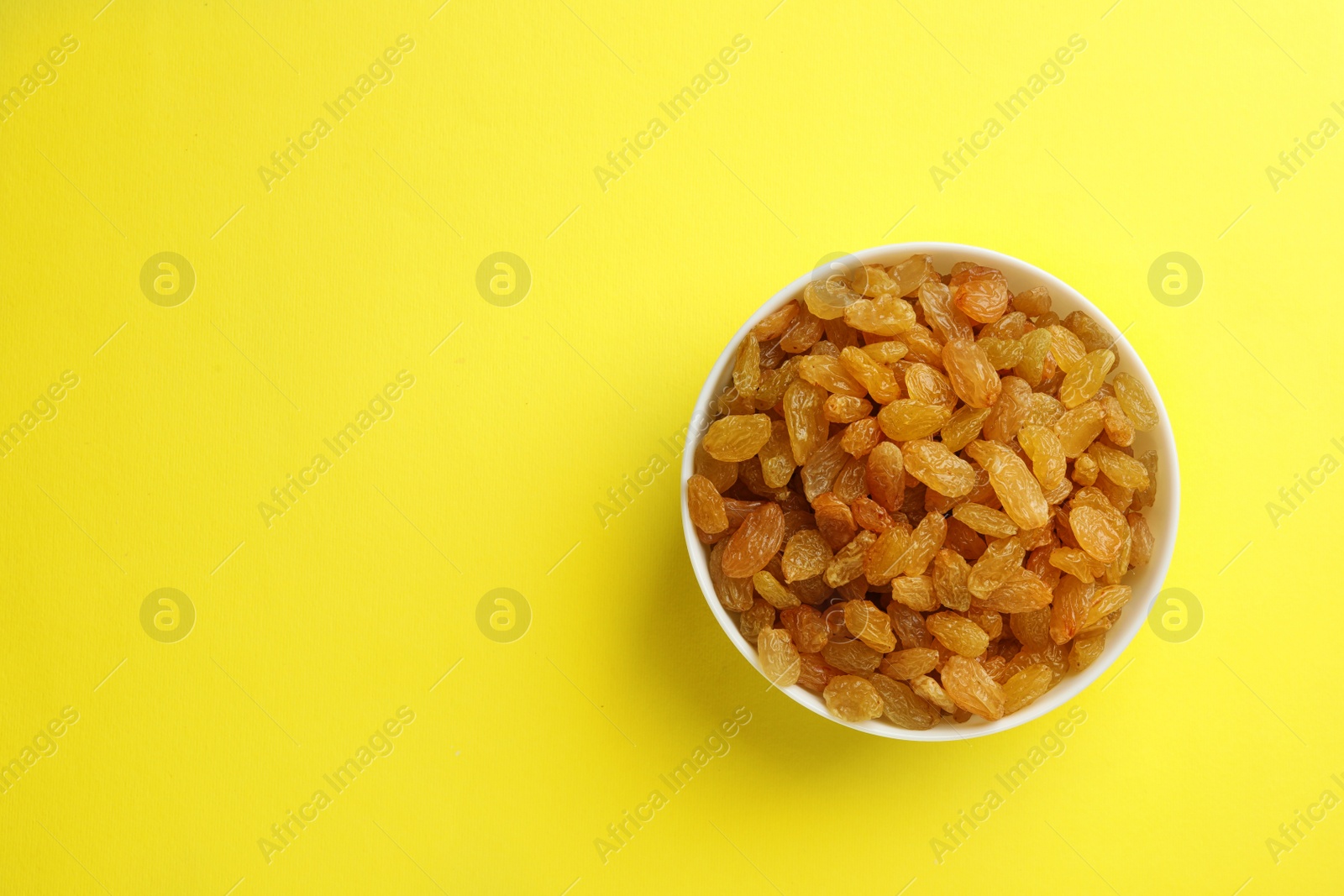 Photo of Bowl with raisins and space for text on color background, top view. Dried fruit as healthy snack