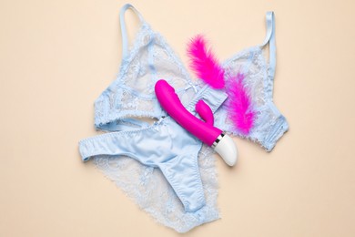 Photo of Vaginal vibrator, feathers and lingerie on beige background, flat lay