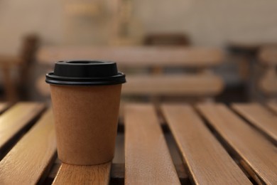 Takeaway paper cup with coffee on wooden table indoors, closeup. Space for text