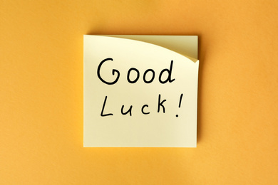 Photo of Note with phrase GOOD LUCK on orange background, top view