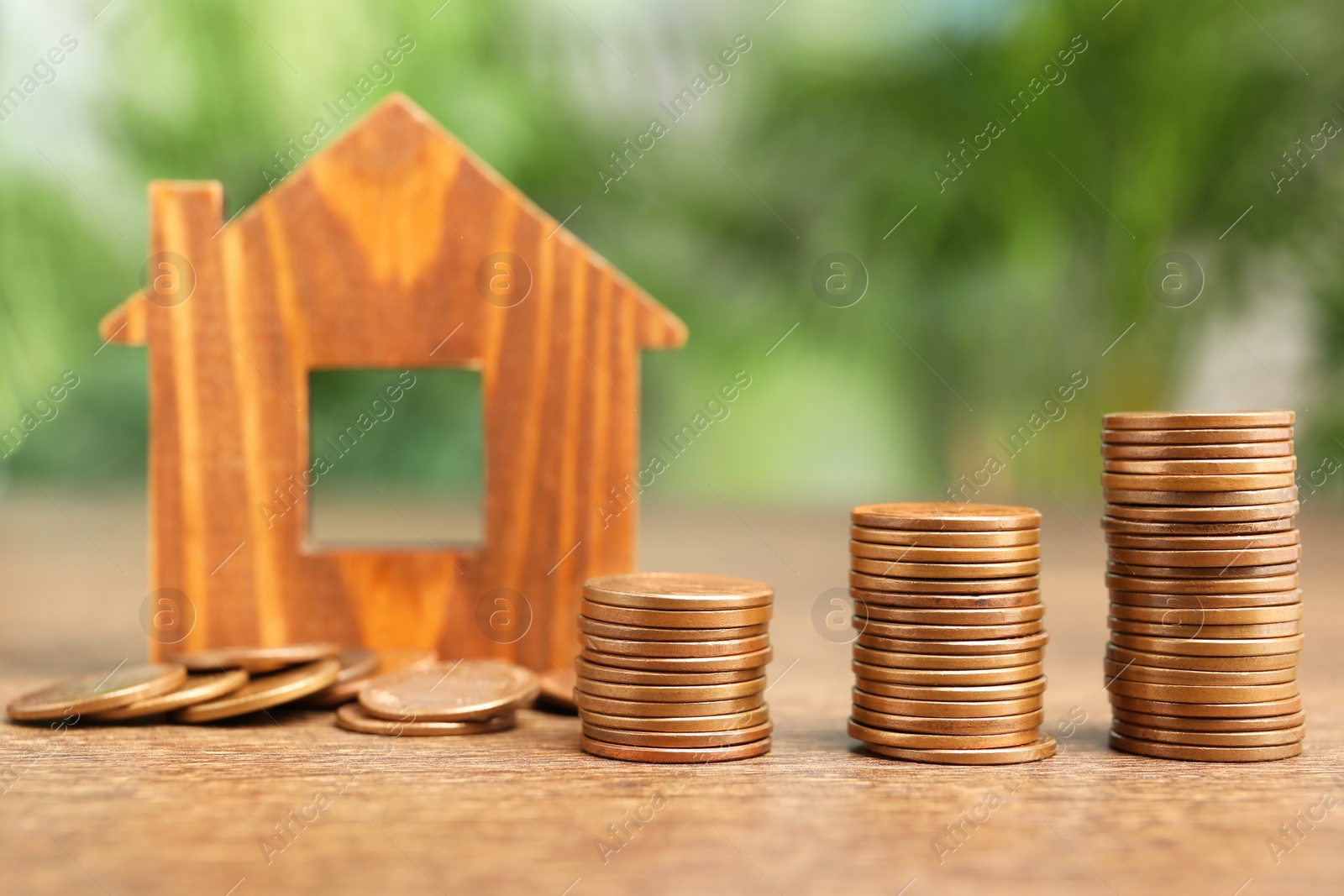 Photo of Mortgage concept. House model and stacks of coins on wooden table against blurred green background