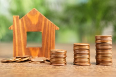 Mortgage concept. House model and stacks of coins on wooden table against blurred green background