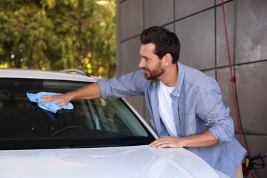 Photo of Bearded man cleaning car windshield with rag outdoors