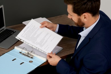 Photo of Businessman putting document into file folder at wooden table in office