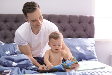 Photo of Young father reading book with his cute little son on bed