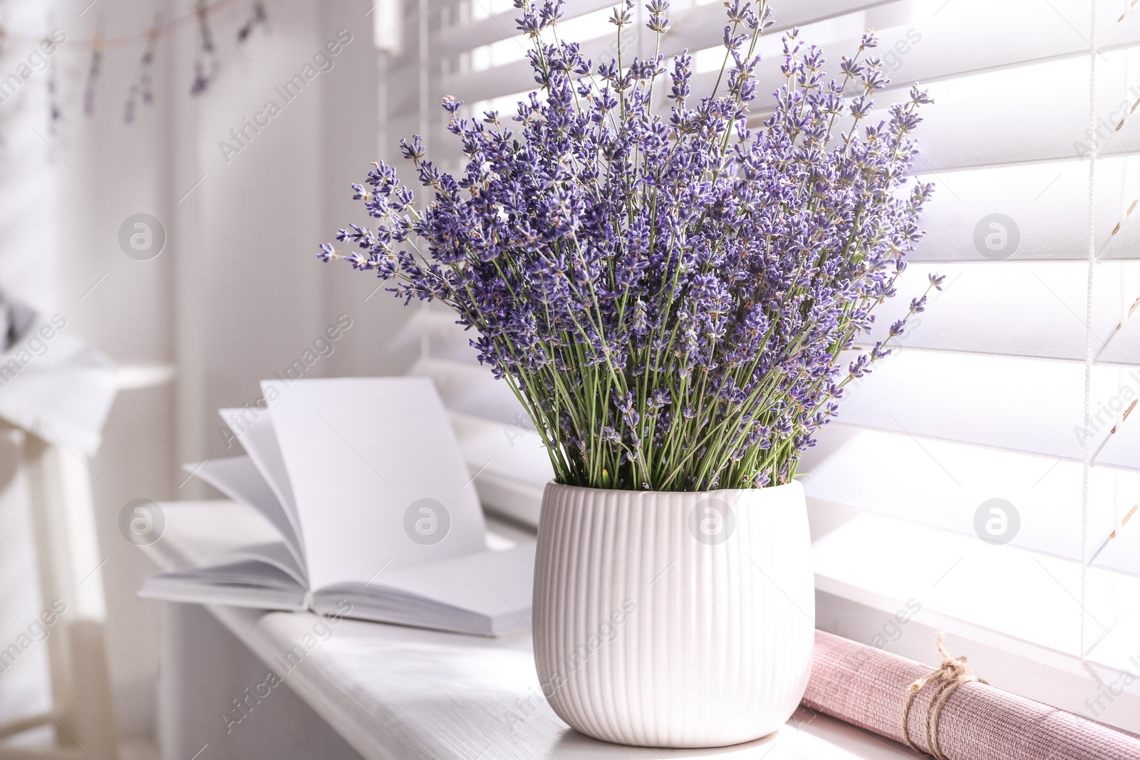 Photo of Beautiful lavender flowers and book on window sill indoors