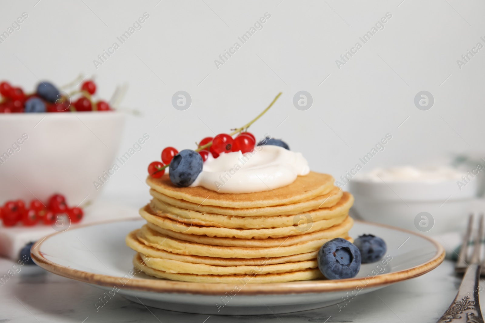 Photo of Tasty pancakes with natural yogurt, blueberries and red currants on marble table