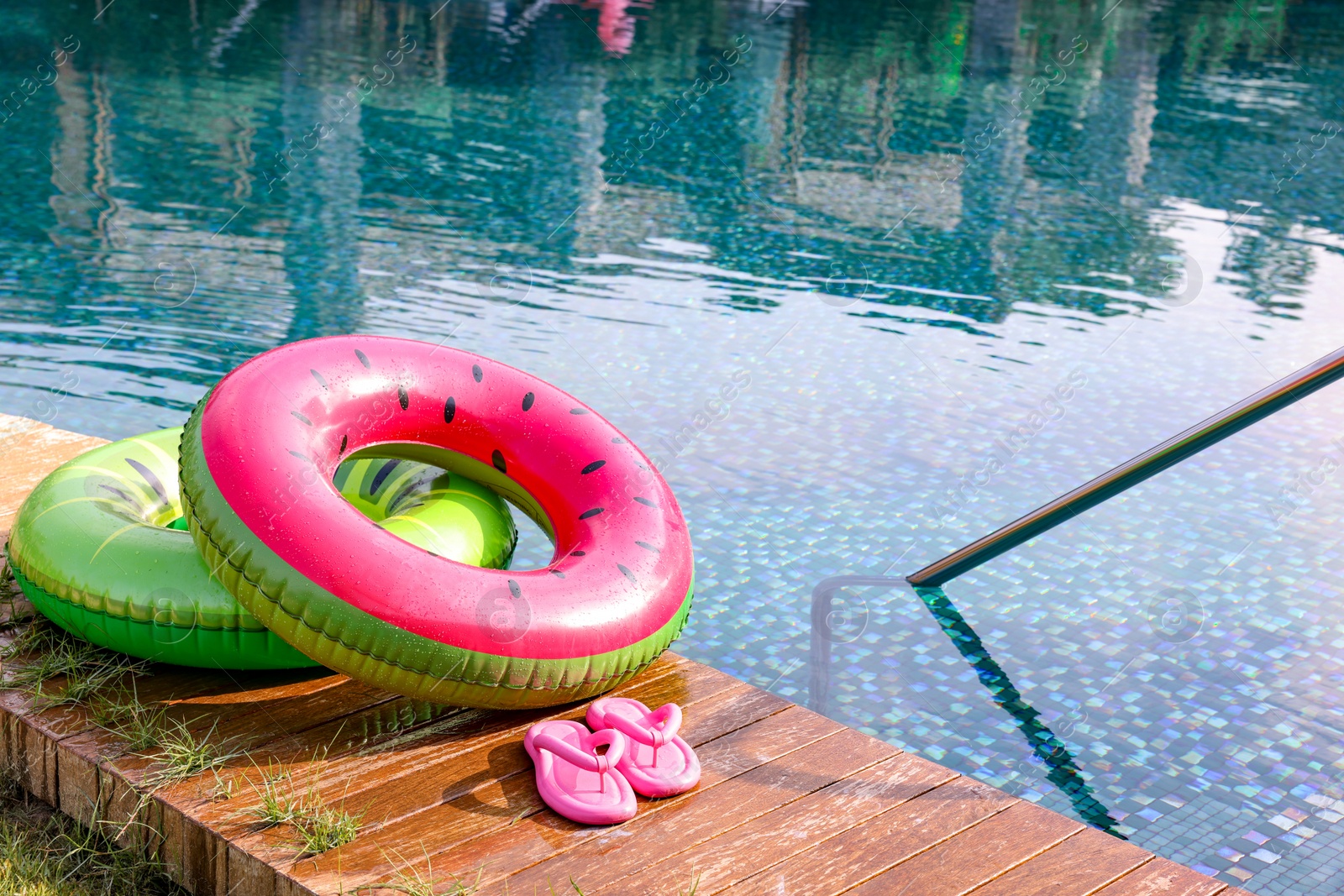 Photo of Inflatable rings and flip flops on wooden deck near swimming pool. Luxury resort