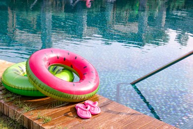 Inflatable rings and flip flops on wooden deck near swimming pool. Luxury resort