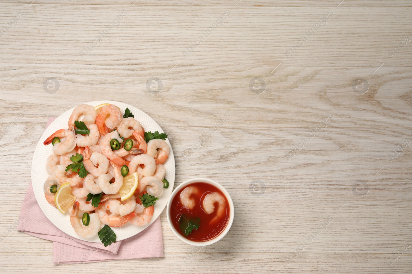 Photo of Tasty boiled shrimps with cocktail sauce, chili, parsley and lemon on light wooden table, flat lay. Space for text