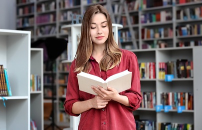 Photo of Young woman reading book in modern library