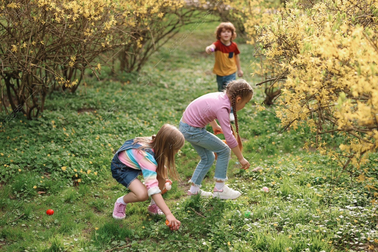 Photo of Easter celebration. Cute little children hunting eggs outdoors