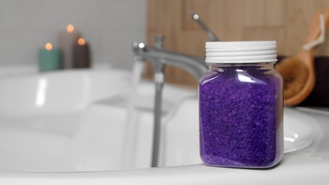 Photo of Jar with purple sea salt on bath. Space for text