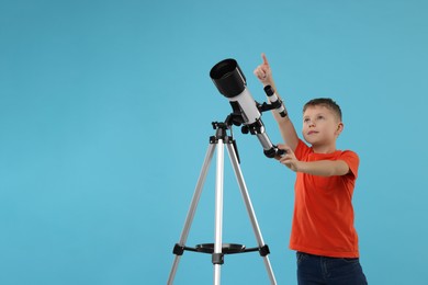 Photo of Cute little boy with telescope pointing at something on light blue background, space for text